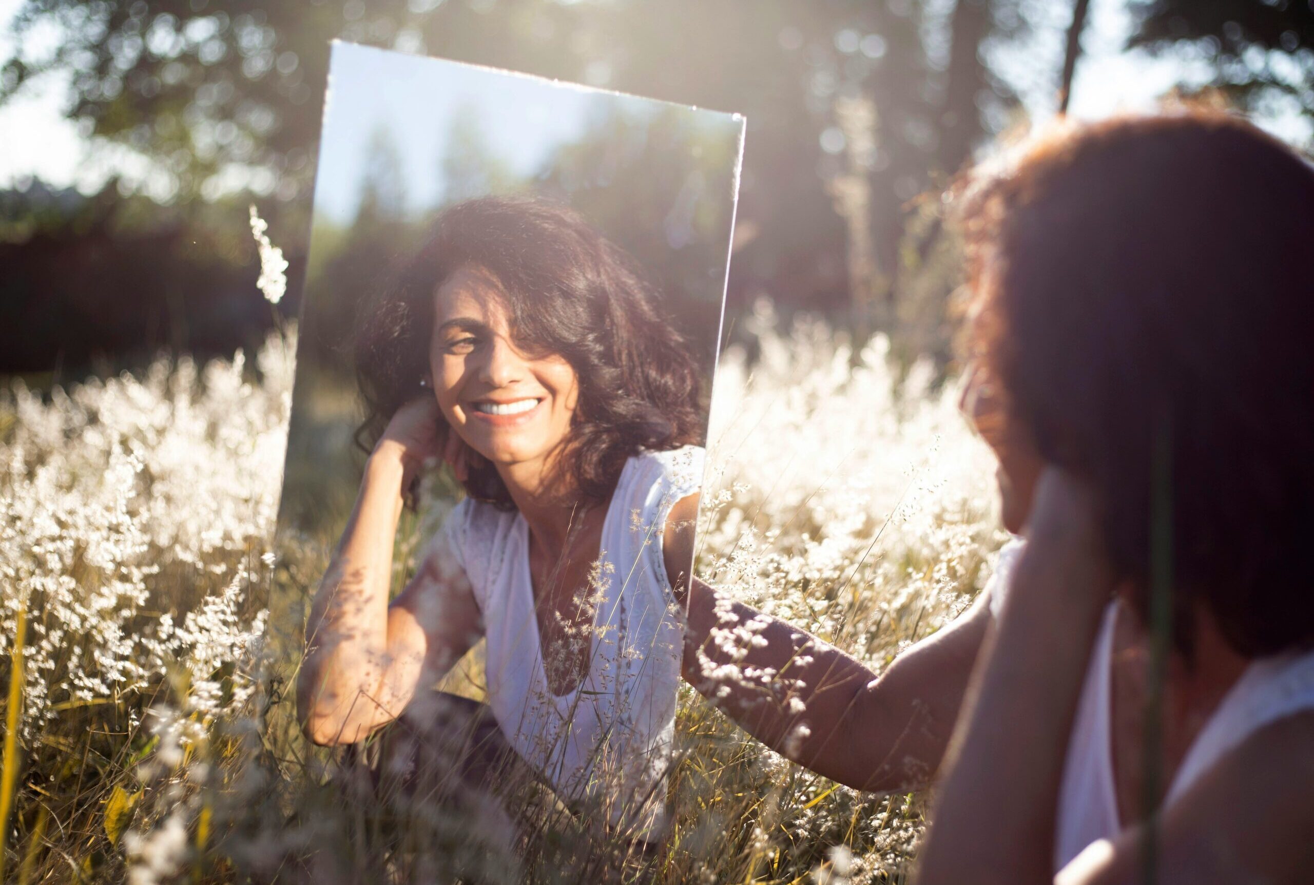 Woman looking at reflection while sitting in field.