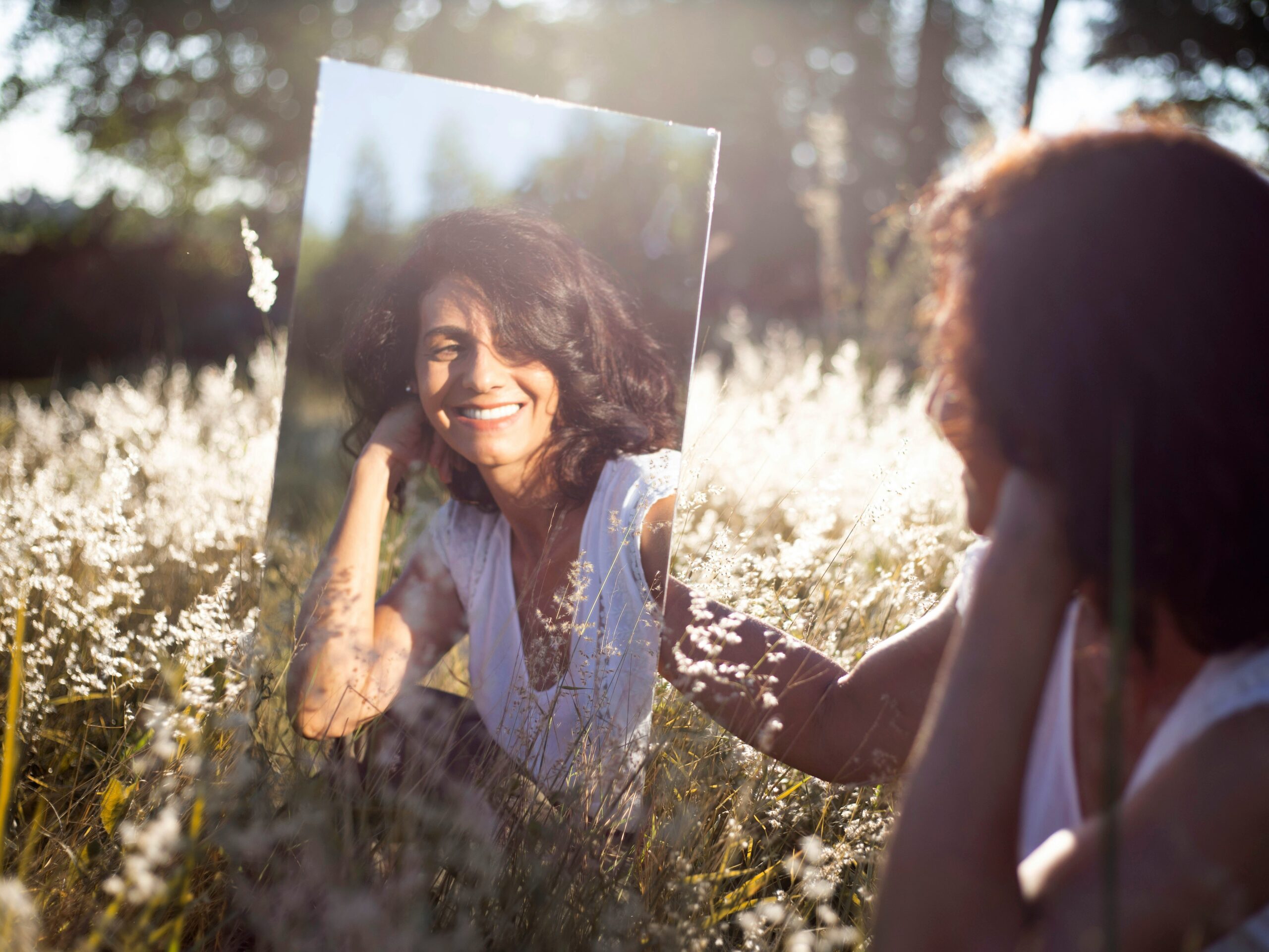Woman looking at reflection while sitting in field.