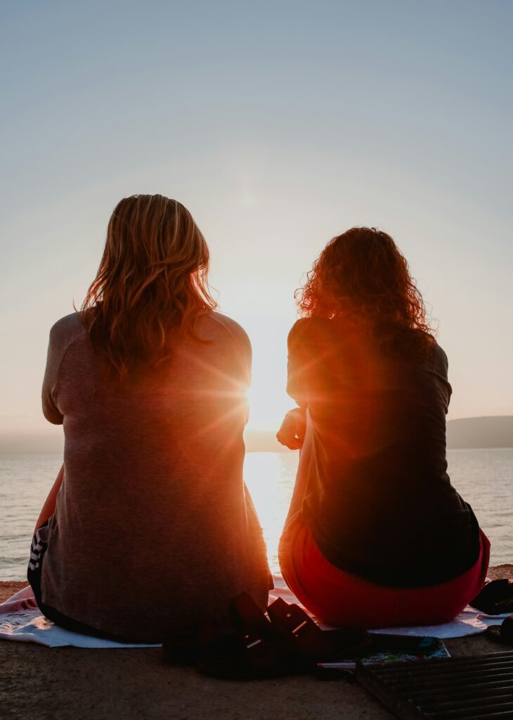 Two friends discussing emotions while watching sunset over lake.