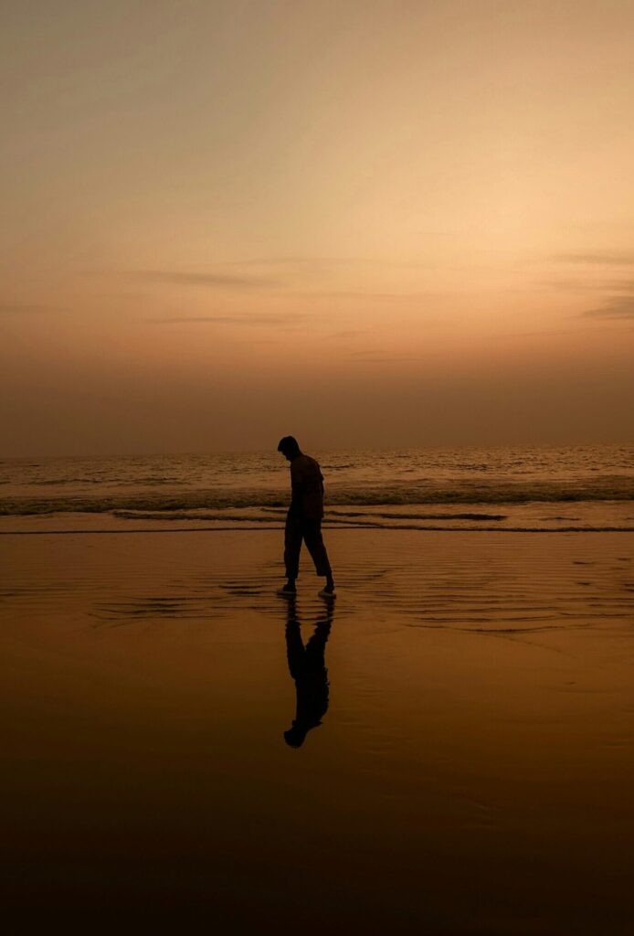 Reflective man walking on beach during sunset.